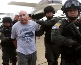 Paul Le Roux, a suspect, jest prowadzony przez uzbrojonych funkcjonariuszy w pobliżu samolotu.