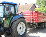 Rolnik z prawem jazdy na ciągnik prowadzi maszynę z czerwoną przyczepą.
