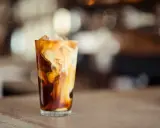 Ein Glas mit Eiswürfeln und einem cremigen Strudel aus Milch und Kaffee. Ein erfrischender Cold Brew Latte.