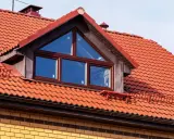 Ein Dachfenster mit dreieckigem Oberlicht und roten Ziegeln. Informieren Sie sich, was kostet eine gaube für Ihr Haus.