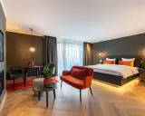 Modern Hotelzimmer mit großem Bett, orangefarbenem Sofa und Sitzbereich.