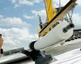 Excavadora descarga un rollo de lámina bentonita. Obreros trabajan en la instalación bajo un cielo nublado.