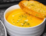 Bol de soupe orange crémeuse garni d'herbes et d'une tranche de pain à l'ail.