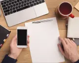 Przygotowuję formalny list. Na biurku leży laptop, telefon, kubek z herbatą i notatnik.