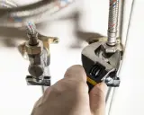 Main tenant resserre un raccord sur un tuyau souple avec une clé.
