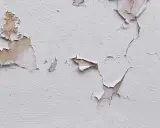 Texture d'un mur où la peinture se décolle comme du plastique, révélant des couches anciennes et la texture du plâtre.