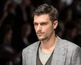 Uomo con capelli spettinati, sguardo intenso, indossa una giacca a quadri grigia.