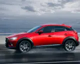 Un Mazda CX-3 rojo circula por una carretera mojada junto al mar. Las medidas del Mazda CX-3 son ideales para la ciudad y la aventura.