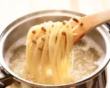 Une louche en bois retire des spaghettis bouillis à la perfection, juste al dente, d'une casserole d'eau bouillante.