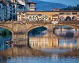 Le Ponte Vecchio à Florence, avec ses maisons colorées et ses reflets sur l'Arno. Une barque navigue paisiblement sous le pont.
