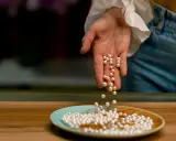 Main d'une personne versant des perles de culture sur une assiette. Apprenez comment nettoyer les perles de culture pour qu'elles brillent.