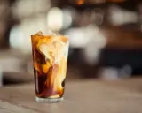 Ein Glas mit Eiswürfeln und cremiger Milch, die sich in dunklem Kaffee wirbelt. Perfekt für die Zubereitung von Cold Brew Coffee.