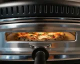En perfekt vedugnsbakad pizza med bubblig kant och färska örter gräddas i en modern ugn.