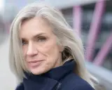 Donna con capelli bianchi e occhi azzurri, indossa un cappotto blu scuro. Un esempio di come vestirsi con i capelli bianchi.