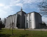 Nowoczesny kościół w Warszowicach, z charakterystycznymi pionowymi żłobieniami na fasadzie, pod błękitnym niebem.