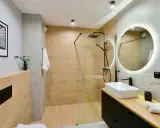 Baño moderno con ducha de suelo continuo, lavabo sobre encimera y espejo circular iluminado.