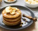 Pila de tortitas americanas con plátano y nueces, bañadas en sirope. Un desayuno perfecto.