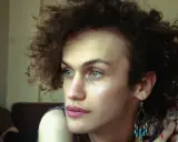Portret osoby z kręconymi włosami, która zastanawia się nad przyczynami dysforii płciowej.