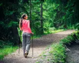Kvinna går med stavar på en grusväg i en grönskande skog.