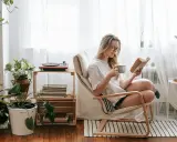 Mujer leyendo en un sillón, taza en mano, rodeada de plantas y libros. Un rincón de lectura con decoración acogedora y un tocadiscos.