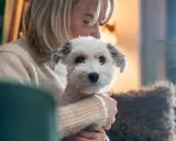 En kvinna håller en vit hund. Hunden ser lite orolig ut, kanske en omplacering hund som anpassar sig.