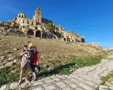 Coppia con cane visita le suggestive rovine di Craco vecchia, un borgo fantasma sotto un cielo azzurro.