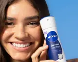 Donna sorridente con prodotto Nivea Derma Control, ideale per chi soffre di bruciore sotto le ascelle.