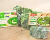 Gefrorener Rahmspinat von Frosta und Iglo, reich an Spinat Protein, liegt auf einem Holzbrett.