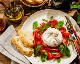 Pyszny ser burrata jak jeść: kremowy ser, pomidory, bazylia i chrupiące pieczywo. Idealne połączenie smaków.