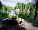 En mysig eldstad med bänkar vid en stilla sjö, omgiven av grönskande skog. Ett perfekt utflyktsmål i Dalarna för avkoppling.