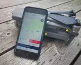 Eine Drohne liegt neben einem Smartphone, auf dem eine Drohnen-App mit Karte und Flugverboten angezeigt wird.