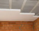 Ocieplenie stropu styropianem w trakcie budowy. Białe płyty styropianowe montowane do betonowych belek stropowych, widoczne ceglane ściany.