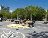 Barcelona autofrei: Menschen genießen einen grünen Platz mit Bäumen in großen Kübeln, Sitzgelegenheiten und einem Spielbereich auf dem Boden.