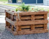 Kwadratowy kwietnik z palet, wypełniony zielenią i pomarańczowymi kwiatami, stanowi ekologiczny element ogrodu.