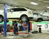 Mecánico trabajando en un taller con vehículos elevados, usando herramientas para neumáticos y otros equipos.