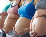 Fyra gravida kvinnor står sida vid sida och håller sina magar. En av dem, andfådd gravid, ler.