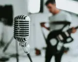 Retro mikrofon gotowy do uchwycenia niskich tonów głosu śpiewaka, podczas gdy w tle muzyk gra na gitarze.