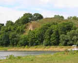 Zielona skarpa nad rzeką, na szczycie której widać ścieżki i ogrodzenie. To góra zamkowa w Drohiczynie, miejsce pełne historii.