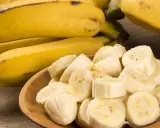 Kawałki bananów w drewnianej misce obok całych owoców. Te żółte banany, bogate w potas, są świetne dla zdrowia nerek.