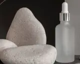 Minimalistyczna fotografia produktu: matowa buteleczka z pipetą i kamienie, tworzące spokojną kompozycję.