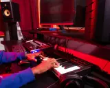 Les mains d'une personne jouent sur un clavier, entourées d'équipement de studio, un rêve de devenir beatmaker.