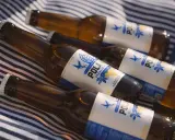 Butelki piwa POLAN z napisem "BEZALKOHOLOWE" leżą na kocu w paski. To piwo ma 0 alkoholu, idealne na upalne dni.