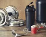 Pesas, batidora y cuchara con proteína en polvo. Ideal para saber cuándo tomar batido de proteínas y optimizar tu entrenamiento.