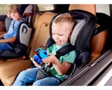 Uśmiechnięty chłopiec bawi się zabawką w foteliku Kinderkraft Comfort Up ADAC. Obok siedzi starszy brat.