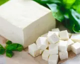 Kostka tofu i pokrojone w kostkę tofu na desce, ozdobione zielonymi liśćmi.