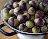 A colander full of purple and green tomatillos, ready for harvest. Their papery husks are partially peeled back, revealing the vibrant fruit within.