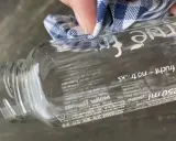 Mit einem Tuch wird das "true fruits" Schrift entfernt. Die Flasche ist aus Glas und hat einen Pfandaufdruck.