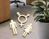 Holzfiguren von Mann, Frau und Transgender-Symbol liegen auf dem Boden. Ein Zeichen für fußgänger gendern.
