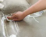 Ręka szoruje szczotką zaplamioną wykładzinę dywanową, tworząc pianę.
