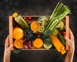 Skrzynka pełna świeżych owoców i warzyw, idealne jedzenie na wyjazd bez lodówki. Znajdziesz tu pomarańcze, winogrona, truskawki, brokuły, seler, ogórka i butelki z sokami.